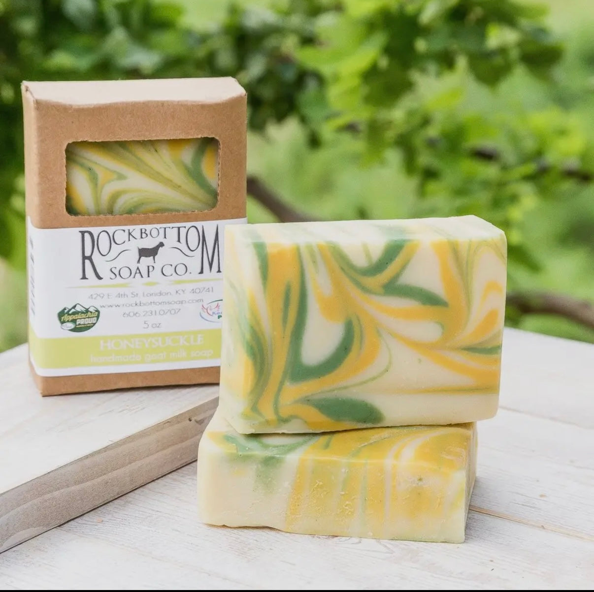 Two bars of swirled yellow and green soap with a Rockbottom Soap Co. box on a wooden surface with a blurred green background.