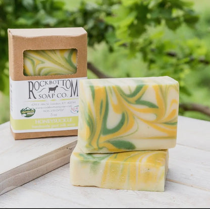Two bars of swirled yellow and green soap with a Rockbottom Soap Co. box on a wooden surface with a blurred green background.