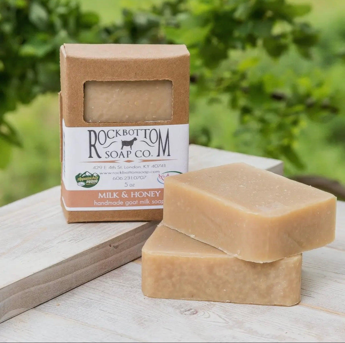 Two bars of soap and their packaging on a wooden surface with a natural background