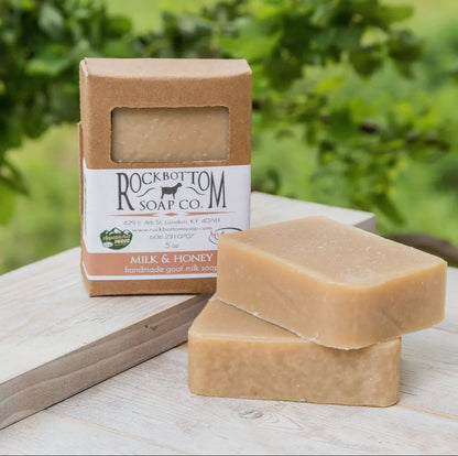 Two bars of soap and their packaging on a wooden surface with a natural background